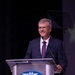 A middle-aged man with gray hair and glasses is speaking at a podium during a formal event. The podium displays the AFA (Air Force Association) logo, indicating this is an official AFA function or conference. The speaker is smiling and appears engaged with the audience.