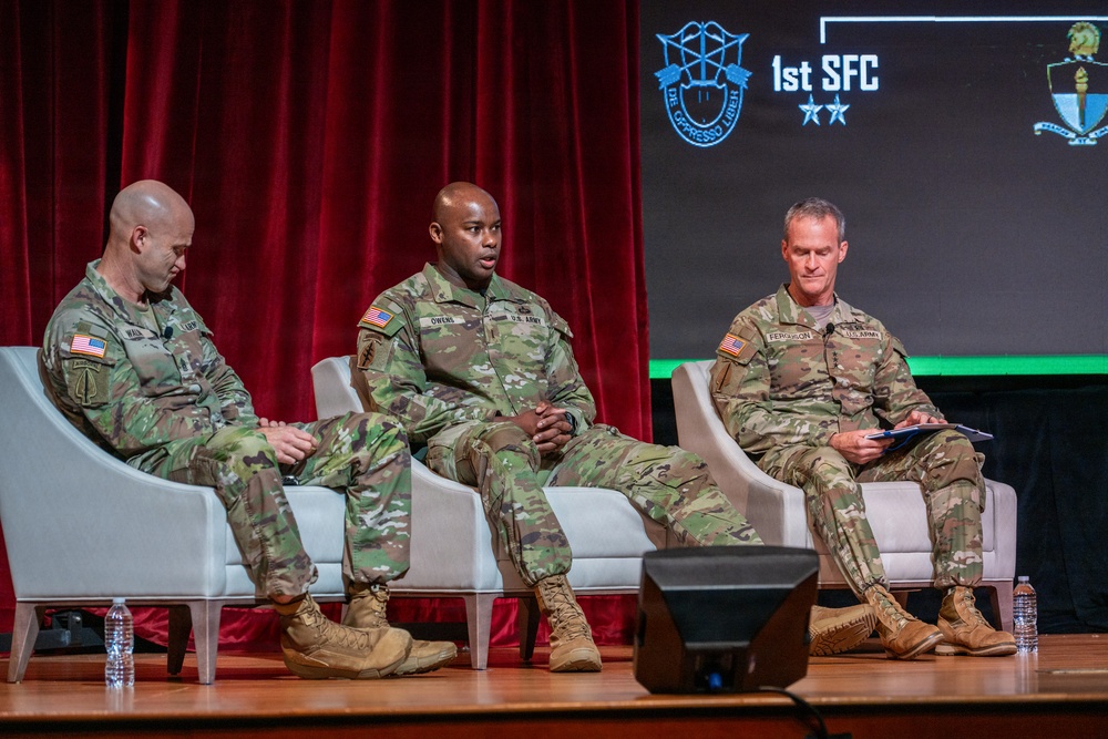 Three U.S. Army soldiers in OCP (Operational Camouflage Pattern) uniforms are seated in white chairs on a stage during a panel discussion or briefing. The backdrop displays the '1st SFC' (1st Special Forces Command) logo with two stars and the motto 'De Oppresso Liber.' Name tapes visible on the uniforms include 'Owens' (center) and 'Ferguson' (right).
