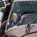 A man is inspecting or working on the interior of an aircraft cockpit from inside, visible through the curved glass canopy. The aircraft appears to be a vintage or historical military aircraft undergoing restoration or maintenance in a large hangar facility. The fuselage bears the marking 'H306' and shows riveted metal construction typical of mid-20th century aircraft.