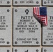 The image shows three military memorial grave markers at what appears to be a national cemetery. The center marker has a small American flag placed on it. All three markers honor veterans from different conflicts, including World War II and Vietnam.