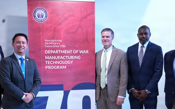 Five men in business attire pose for a group photo in front of a promotional banner for the Department of War Manufacturing Technology Program, celebrating its 70th anniversary since 1956. The setting appears to be an indoor facility or conference space. The occasion appears to be an official or commemorative event related to the program's milestone anniversary.