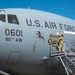 A U.S. Air Force military transport aircraft, tail number 0601 assigned to the 911th Airlift Wing, is being decorated with nose art bearing the name 'Roberto Clemente'. A service member in camouflage uniform is standing on a mobile staircase applying or unveiling the artwork on the fuselage. The image is taken on a clear, sunny day on what appears to be a flight line or tarmac.