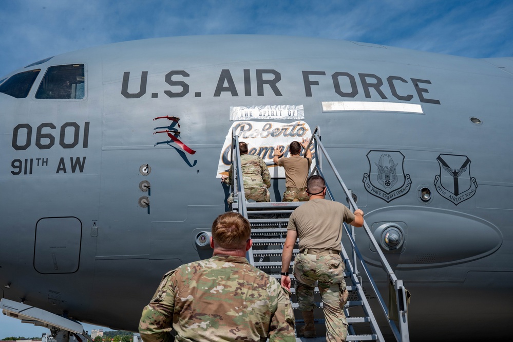 U.S. Air Force personnel from the 911th Airlift Wing are applying or unveiling nose art on a military transport aircraft (tail number 0601). The nose art reads 'The Spirit of Roberto Clemente,' honoring the legendary Pittsburgh Pirates baseball player. The ceremony appears to be taking place on a flight line during daylight hours.