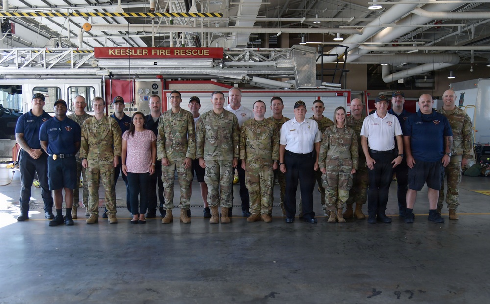 A group photo taken inside the Keesler Fire Rescue station, showing approximately 20-25 individuals including military personnel in camouflage uniforms, civilian fire rescue staff in white shirts, and other personnel. The group is posed in front of a red fire apparatus with the 'Keesler Fire Rescue' sign visible overhead. This appears to be an official visit or joint training event at Keesler Air Force Base in Mississippi.