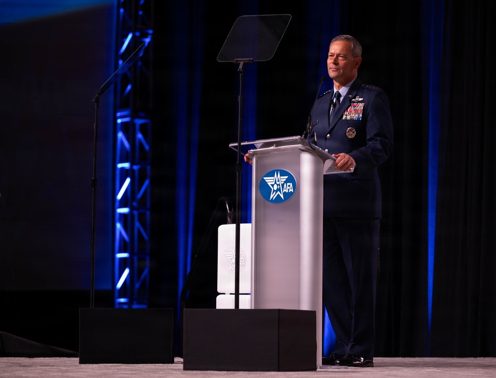 A senior U.S. Air Force officer in dress uniform is delivering a speech at a podium bearing the AFA (Air Force Association) logo. The event appears to be a formal military or defense industry conference held in a large venue with professional stage lighting. The officer displays numerous service ribbons and rank insignia consistent with a general officer.