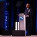 A senior U.S. Air Force officer in dress uniform is delivering a speech at a podium bearing the AFA (Air Force Association) logo. The event appears to be a formal military or defense industry conference held in a large venue with professional stage lighting. The officer displays numerous service ribbons and rank insignia consistent with a general officer.