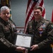 Two U.S. Army soldiers in dress green uniforms are posing together holding a framed Purple Heart certificate during a formal military award ceremony. The soldier on the right is wearing a Purple Heart medal on his chest, indicating he is the recipient. Both soldiers display Special Forces (Airborne) insignia and extensive service ribbons.