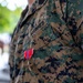 A close-up photograph of a U.S. Marines service member wearing the MARPAT (Marine Pattern) digital camouflage uniform (MCCUU). A Bronze Star Medal with ribbon is pinned to the left chest pocket, and the Eagle, Globe, and Anchor (EGA) emblem is embroidered on the pocket flap. The individual is holding a red folder or binder at their side.