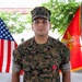 A U.S. Marine identified by name tape as 'FIGUEROA' stands at attention in Marine Pattern (MARPAT) woodland camouflage uniform. He is wearing a Bronze Star Medal with Valor device on his chest, indicating a formal award ceremony. An American flag and a U.S. Marine Corps flag are visible in the background.