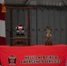 A memorial display at Nellis AFB Fire &amp; Emergency Services features a firefighter's helmet marked '343' and '9-11-2001' mounted on a wooden stand with a fire axe, commemorating the 343 FDNY firefighters lost on September 11, 2001. A decorative brass bell on a wooden base sits alongside the helmet display. Both items rest on a red tablecloth bearing the Nellis AFB Fire &amp; Emergency Services insignia and text.