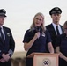 Four airline crew members are gathered at a podium during what appears to be a formal outdoor ceremony or press event. A woman in a navy flight attendant uniform is speaking into a microphone at the lectern, flanked by two pilots in uniform caps and another flight attendant. The group's solemn expressions suggest this may be a memorial or serious official address.