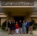A group of eight people pose for a formal group photograph in front of the Moody Field Club building. The building features a prominent sign reading 'MOODY FIELD CLUB' above a covered entrance portico. The group appears to be gathered for an official or commemorative occasion.