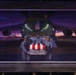 A framed painting displayed on an easel depicting a military dignified transfer ceremony at an airfield. The artwork shows uniformed service members carrying a flag-draped transfer case from the rear cargo bay of a large military transport aircraft at dusk or dawn. The painting uses dramatic purple and orange tones to convey a solemn, ceremonial atmosphere.