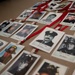 The image shows a memorial display featuring numerous ID badge-style photographs of firefighters and first responders laid out on a flat surface. Each photo is attached to a red lanyard and clipped with a small wooden clothespin, with handwritten names visible beneath each image. The display appears to be a tribute or remembrance collection honoring fallen or notable emergency service personnel.