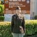 A U.S. Army soldier wearing the Army Service Uniform (ASU) in olive green stands smiling in front of a headquarters sign. The sign reads 'Two Nations, One Team' and identifies the location as Headquarters, Material Support Command-Korea, 19th Expeditionary Sustainment Command, 8th Army. The soldier displays a name tape reading 'LEE,' service ribbons, medals, and unit patches.