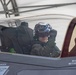 A military pilot is seated in the cockpit of what appears to be an F-35 Lightning II fighter jet, wearing a helmet-mounted display system with visible blue optical sensors. The canopy is open and the pilot appears to be conducting pre-flight checks or preparing for a mission. Warning labels including 'DANGER - EJECTION SEAT' and 'WARNING - DO NOT WITHIN 3 INCHES O[F]' are clearly visible on the aircraft fuselage.
