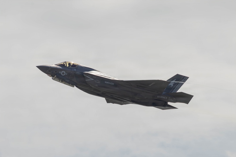 A U.S. Marine Corps F-35B stealth fighter jet is captured in flight against an overcast sky. The aircraft belongs to VMFA-533 (Marine Fighter Attack Squadron 533) as indicated by markings on the fuselage. The jet appears to be in level flight, possibly during an airshow or training exercise.