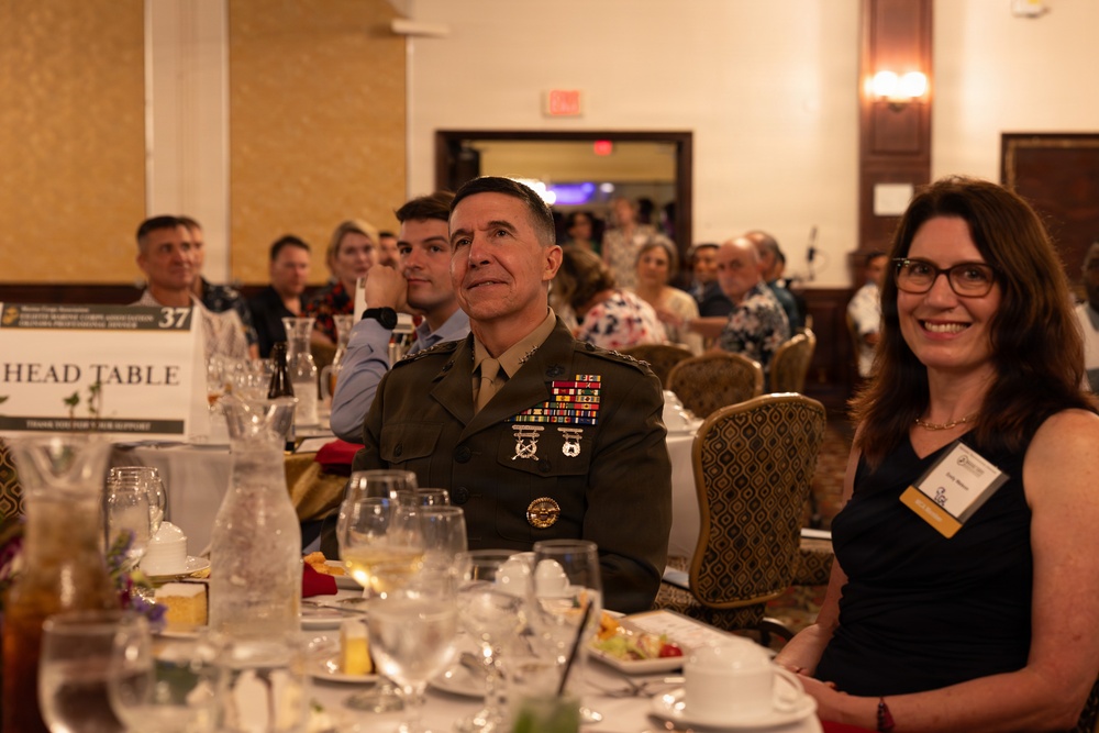 A formal military banquet or awards dinner taking place in a hotel ballroom. A senior military officer in dress uniform with multiple service ribbons and medals is seated at the 'Head Table' alongside civilian attendees. The event appears to be a professional or organizational recognition ceremony.