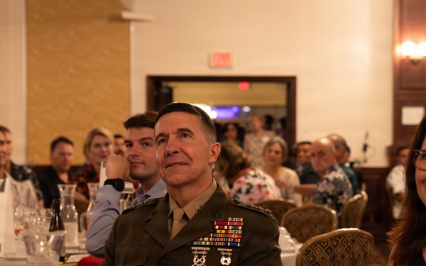 A formal military banquet or awards dinner taking place in a hotel ballroom. A senior military officer in dress uniform with multiple service ribbons and medals is seated at the 'Head Table' alongside civilian attendees. The event appears to be a professional or organizational recognition ceremony.
