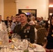 A formal military banquet or awards dinner taking place in a hotel ballroom. A senior military officer in dress uniform with multiple service ribbons and medals is seated at the 'Head Table' alongside civilian attendees. The event appears to be a professional or organizational recognition ceremony.