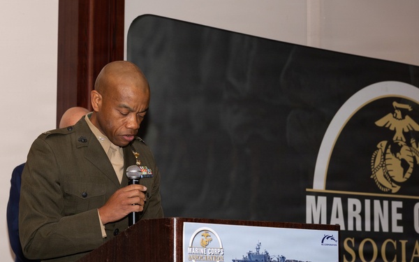 A U.S. Marine Corps officer in service uniform is speaking at a podium during the Marine Corps Association Okinawa Professional Dinner. The event banner behind him displays the Marine Corps Association logo and the text 'EST 1913' along with 'Supporting Today's Marines'. A sign on the podium identifies this as the 'Okinawa Professional Dinner' and features imagery of amphibious military operations.