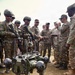 A group of military personnel from what appears to be Indian Army and US Army forces are gathered around a quadruped military robot labeled 'SIMBA'. The robot is a four-legged autonomous ground vehicle painted in olive/dark green, equipped with sensors and cameras. A soldier appears to be demonstrating or operating the robot using a handheld controller.