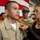 USS Tripoli Chief Pinning A military promotion or award ceremony is taking place, likely in a naval or Marine Corps setting. A woman in civilian clothing is pinning an insignia or device onto the collar of a service member in a tan/khaki uniform. An American flag and additional uniformed personnel are visible in the background.