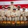 USS Tripoli Chief Pinning A group of eight U.S. Navy Chief Petty Officers pose for a formal group photograph in front of an American flag backdrop. They are dressed in khaki service uniforms with combination covers (white-topped caps) and display various ribbons and warfare devices. In front of them are seven decorative wooden boxes featuring Japanese-style artwork with kanji characters and sunrise/Mount Fuji imagery.