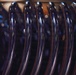 The image shows a close-up macro photograph of multiple clothes hangers lined up in a row. The hangers appear to be dark navy or black plastic with a glossy finish, reflecting ambient light as circular bokeh highlights. The shallow depth of field creates a blurred background while keeping the foreground hangers in sharp focus.