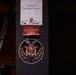 The image shows a dark surface, likely a music stand or equipment case, with three stickers/labels affixed to it. The labels represent different musical organizations: the Mozarteum Orchester Salzburg, the Gewandhaus Orchester, and the U.S. 7th Fleet Band. A handwritten date '5. 2006' is visible on the Mozarteum label.