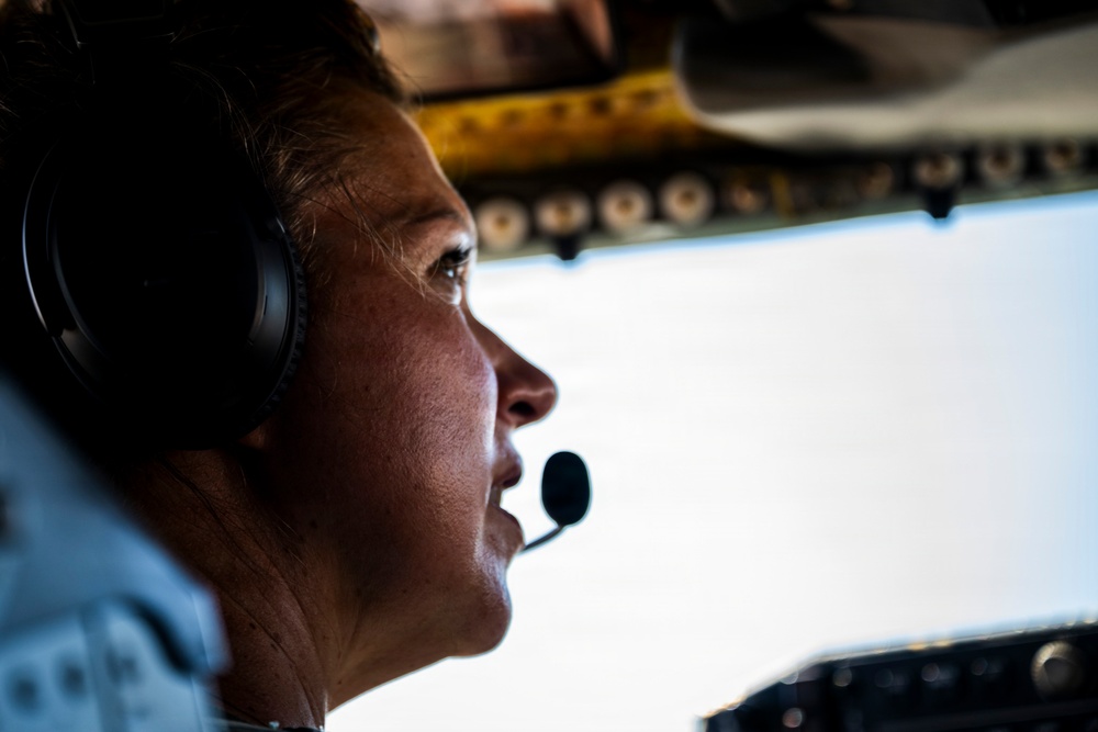 A close-up profile shot of a pilot seated in an aircraft cockpit, wearing aviation headset with boom microphone. The image is dramatically lit with strong contrast between shadow and light, capturing the pilot gazing forward through the cockpit windshield. Overhead cockpit panels with switches and yellow markings are partially visible in the background.