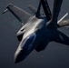 A military fighter jet, identifiable as an F-22 Raptor, is photographed in close proximity to a tanker aircraft during an aerial refueling operation. The tanker's boom and wing are visible in the upper portion of the frame, bearing the markings 'ALASKA' and 'ANG' (Air National Guard) in gold lettering on a dark blue surface. The image is taken from the tanker's perspective looking down at the receiver aircraft.