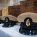 The image shows a ceremonial display of U.S. Navy Chief Petty Officer combination covers (dress caps) arranged on a white-cloth-covered table. Behind each cap is a personalized wooden shadow box or presentation case, with the foremost one inscribed 'CMC(SCW/EXW/TW) SHELBY DIANNE DILLMAN'. This appears to be a Navy Chief Petty Officer pinning or advancement ceremony.