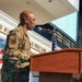 A U.S. Air Force military officer in OCP (Operational Camouflage Pattern) uniform is speaking at a podium with a microphone at the Museum of Aviation. The event appears to be an official military ceremony or address, taking place inside the museum facility. An American flag and what appears to be a unit flag are visible in the background.