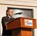 A uniformed official is speaking at a podium bearing the 'Museum of Aviation' logo. The speaker appears to be wearing a dark dress uniform with gold sleeve stripes and insignia, suggesting a military or fire service rank. The setting appears to be a formal event or ceremony held at or associated with the Museum of Aviation.