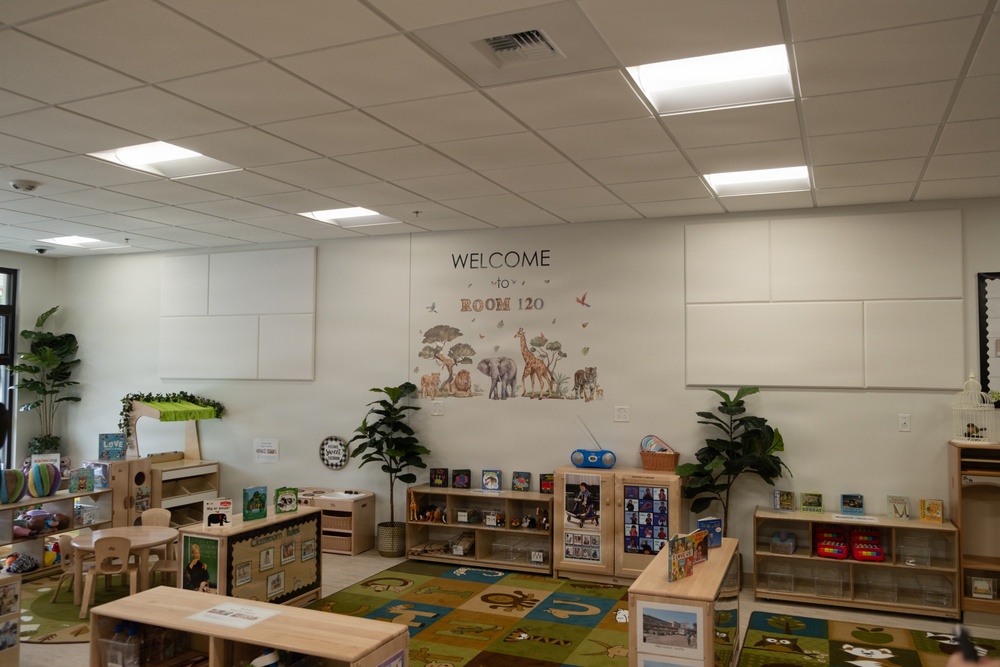 This image shows a well-organized early childhood classroom identified as Room 120. The room features a safari/jungle theme with animal wall decals, colorful educational rugs, and multiple learning stations with wooden furniture. The space appears newly set up or freshly arranged, with no children present.