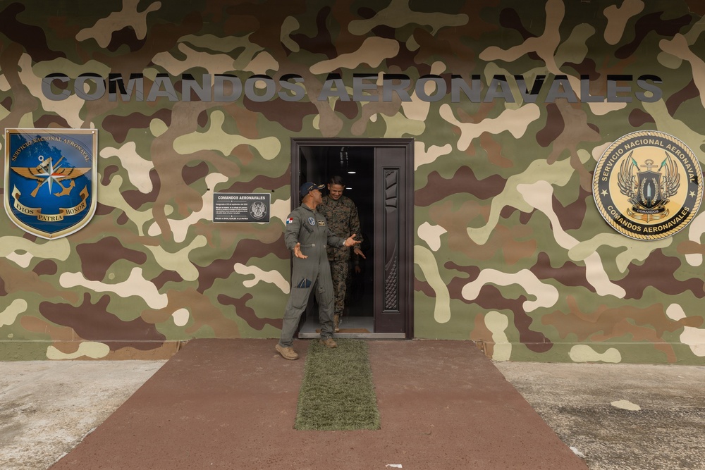 Two military personnel are standing in the doorway of a building belonging to the 'Comandos Aeronavales' (Aeronaval Commandos), part of Panama's Servicio Nacional Aeronaval. The building facade is painted in a woodland camouflage pattern and displays two official unit emblems on either side of the entrance. The individuals appear to be engaged in conversation.