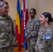 Three U.S. Army soldiers in OCP (Operational Camouflage Pattern) uniforms are engaged in conversation inside a building with multiple national flags in the background. The soldier on the left displays two stars on his chest indicating the rank of Major General, with a name tape reading 'RAAS'. The two soldiers on the right wear KFOR RC-EAST (Kosovo Force Regional Command East) patches, indicating a NATO peacekeeping mission context.