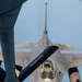 An aerial refueling operation is captured from the perspective of a tanker aircraft looking down at a fighter jet. The receiver aircraft, identifiable as an F-16 Fighting Falcon, is positioned directly below the tanker's refueling boom, which is visible extending diagonally across the frame. The fighter shows signs of heavy use with visible weathering and paint wear on its airframe.
