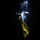 56th CRD Dugway VALEX 2026 A person wearing protective gear including a helmet with a mounted light, a face shield/visor, and blue gloves is working in near-total darkness. They appear to be handling a yellow garment or material, possibly placing it into or removing it from a clear plastic bag or protective covering. The dramatic low-key lighting creates high contrast between the illuminated subject and the dark background.