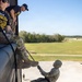 Military personnel are conducting a rappelling training exercise from an elevated structure, likely a rappel tower. An instructor wearing a navy blue shirt with yellow text reading 'INSTRUCTOR' and partial text 'SABALAUSKI' and 'SSAULT SCHOOL' oversees a soldier in full camouflage uniform and helmet descending the wall on a rope. Additional personnel are visible on the ground below, suggesting this is a supervised training event.