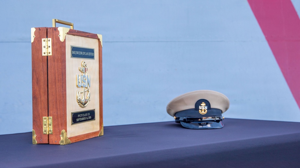 The image shows a formal U.S. Navy Chief Petty Officer promotion ceremony display on a table covered with a dark blue cloth. A decorative wooden keepsake box with brass hardware and a USN anchor emblem is displayed alongside a Chief Petty Officer's combination cover (hat). The plaques on the box reference 'BMC(SW)(EXW) Dylan Jeffers,' 'FY27 Class 133,' and 'September 16, 2026.'