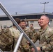 A group of U.S. Army soldiers in Operational Camouflage Pattern (OCP) uniforms are gathered on what appears to be a military installation tarmac or airfield. A senior soldier with the name tape 'RICHTER' is prominently visible on the right, appearing to engage in conversation with fellow soldiers. The setting suggests an arrival, departure, or greeting ceremony near a military building.