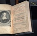 An open antique book displayed on a stand, showing a title page and an engraved portrait frontispiece. The book is 'The Compleat Surveyor' by William Leybourn, fourth edition, printed in London in 1679. The title page features red and black typography typical of 17th-century printing, and the left page contains an engraved oval portrait of the author.