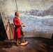 A museum exhibit featuring a wax or animatronic figure dressed in 18th-century colonial attire, standing in a dramatic immersive display with projected imagery of a snowy landscape and historical text. The figure holds a small book or journal and appears to be narrating or recounting a journey. A subtitle on the projection reads 'Our travails continued as we came to,' suggesting this is an interactive or theatrical historical presentation.