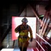 A firefighter in full turnout gear and white helmet is ascending a staircase, framed by a bright red-lit doorway or opening behind them. The image is captured with a zoom burst or radial blur photographic technique, creating a dramatic sense of motion and urgency. The structural elements of what appears to be a training facility or building stairwell are visible around the subject.