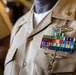 A close-up photograph of a U.S. Navy officer's khaki service uniform showing the chest area with multiple decorations and insignia. The uniform displays a substantial ribbon rack with various awards, two sets of aviation/warfare qualification wings, and collar devices. The image focuses on the decorations and insignia, with the officer's face not visible in the frame.