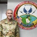 A U.S. Air Force officer in OCP (Operational Camouflage Pattern) uniform stands smiling beside an official unit emblem at Robins Air Force Base. The insignia identifies the location as Robins AFB and references the Installation Contracting Division under AFSC/PZI. The officer's name tape reads 'PESKE' and rank insignia (colonel eagle) is visible on the shoulder.