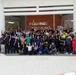 A large group of approximately 60-80 people are posing for a group photograph in front of the Laem Chabang Port building in Thailand. The participants are wearing various uniforms including dark workwear, high-visibility vests, and casual office attire, suggesting a multi-department or multi-organization gathering. Many individuals are raising their fists or giving thumbs-up gestures in a celebratory or solidarity pose.