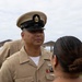 A United States Navy Chief Petty Officer in Service Khaki uniform is engaged in conversation with a civilian woman at what appears to be a beachside location. The sailor is wearing a combination cover with the USN anchor insignia and displays multiple service ribbons and warfare devices on his uniform. The setting appears to be an outdoor ceremony or informal gathering near a beach.
